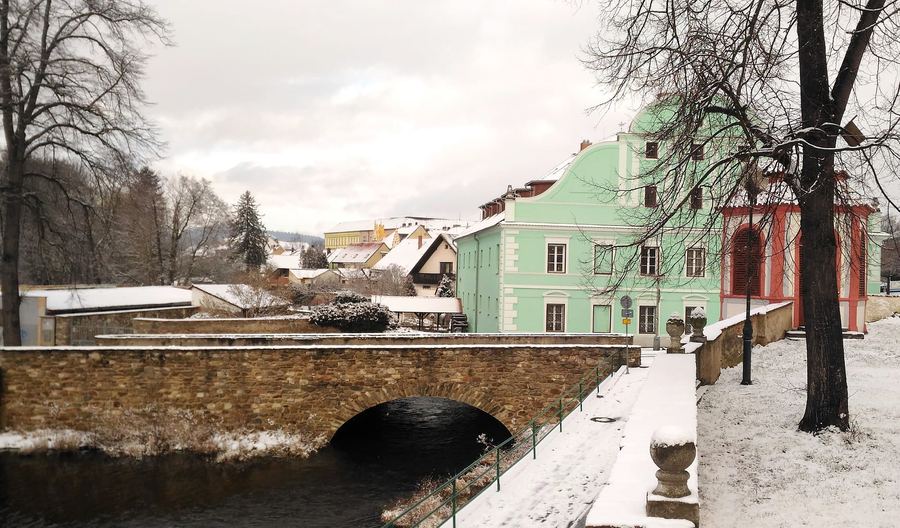 Kamenný most přes Otavu a zelený dům v zasněžené krajině